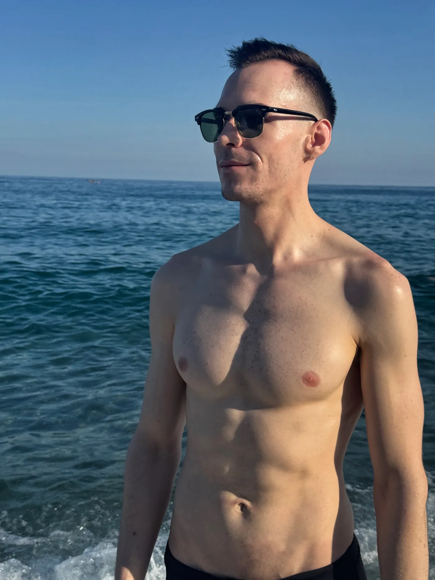 István standing shirtless by the sea, direct gaze