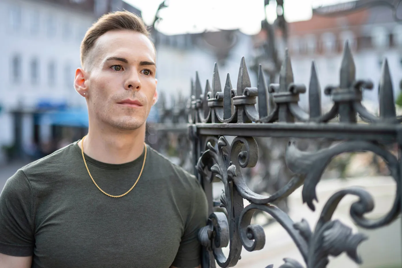 István leaning on an iron fence, looking away